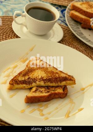 Deux toasts français servis avec du miel sur une assiette blanche pour le petit-déjeuner ou le brunch, en arrière-plan une tasse de café noir et une pile de toasts français. Banque D'Images