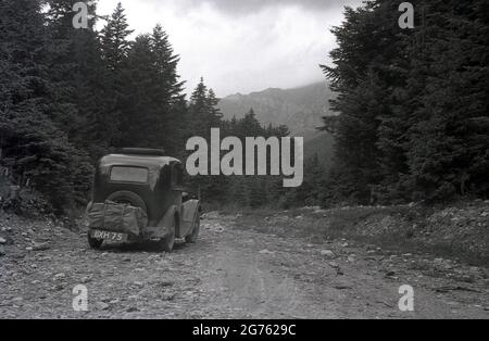 1935, historique, une voiture de l'époque, avec une plaque d'immatriculation britannique, bâillonez une piste rocheuse en gravier en haut d'une zone forestière des montagnes des Sudètes ou des Sudètes, Sudetenland, Tchécoslovaquie. Ils constituent la partie la plus haute de ce que l'on appelle le massif de Bohême, une série de chaînes de montagnes couvrant des parties de l'europe centrale. Banque D'Images