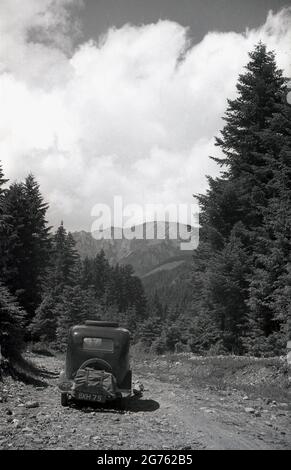 1935, historique, une voiture de l'époque, avec une plaque d'immatriculation britannique, bâillonez une piste rocheuse en gravier en haut d'une zone forestière des montagnes des Sudètes ou des Sudètes, Sudetenland, Tchécoslovaquie. Ils constituent la partie la plus haute de ce que l'on appelle le massif de Bohême, une série de chaînes de montagnes couvrant des parties de l'europe centrale. Banque D'Images