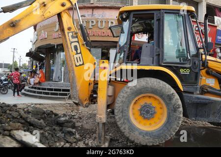 JCB machine de terrassement travaillant sur route. Le chargeur à godet JCB répare une section d'une route de terre. La route est en expansion dans le quartier résidentiel. Thème o Banque D'Images