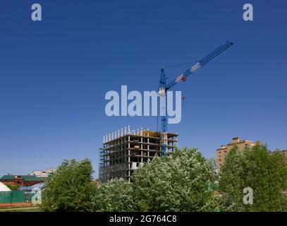 Entre les maisons anciennes et modernes, une grue de tour construit un nouveau bâtiment de plusieurs étages. Concept de construction et de rénovation. Banque D'Images