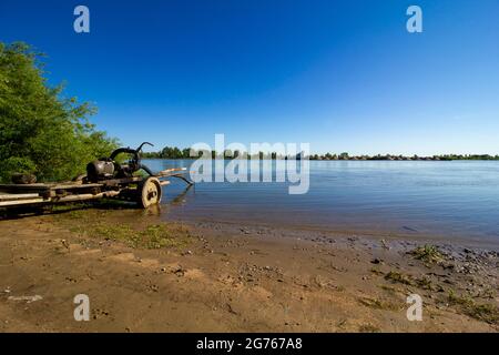 Pompe à eau faite maison tout en travaillant sur le bord de la rivière. Équipement d'arrosage rustique sur fond de rivière avec un bateau flottant. Banque D'Images