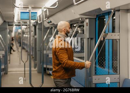 Un homme avec une barbe dans un masque médical pour éviter la propagation du coronavirus se prépare à quitter la voiture de métro tenant la main courante. Un homme chauve Banque D'Images