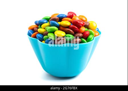 Boutons de chocolat enrobés de bonbons de couleur arc-en-ciel dans un bol bleu amusant sur fond blanc Banque D'Images