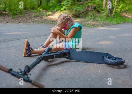 Traumatisme sur le scooter. Une jeune fille de cinq ans est tombée sur un scooter dans un parc et a gravement blessé son genou. Concept de blessure de scooter électrique Banque D'Images