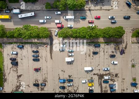 Vue aérienne en haut de la rue animée avec circulation de voitures en mouvement et grand parking avec beaucoup de véhicules garés. Banque D'Images