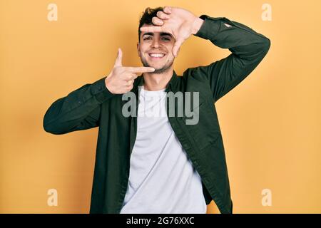 Jeune hispanique portant des vêtements décontractés souriant faisant cadre avec les mains et les doigts avec le visage heureux. Créativité et concept de photographie. Banque D'Images