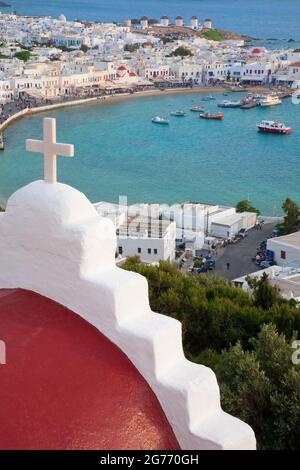 Église en dôme rouge avec croix blanche surplombant la ville de Mykonos et le port sur la côte de la mer Égée dans les îles grecques Banque D'Images
