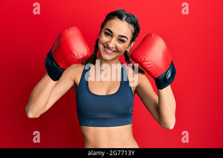 Jeune fille de brunette utilisant des gants de boxe portant des tresses souriant avec un sourire heureux et frais sur le visage. Montrant les dents. Banque D'Images