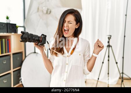 Belle femme caucasienne travaillant comme photographe au studio de photographie en colère et fou criant frustré et furieux, criant avec colère. Rage et Banque D'Images