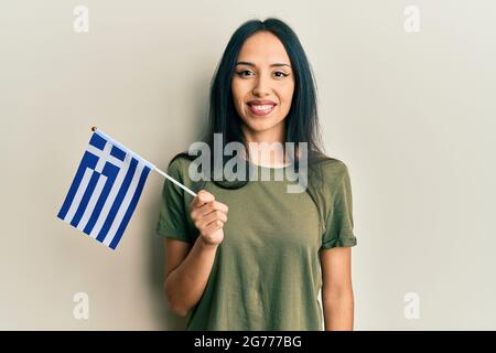 Jeune fille hispanique portant le drapeau de la grèce a l'air positif et heureux debout et souriant avec un sourire confiant montrant des dents Banque D'Images