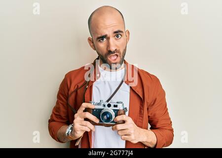 Jeune homme hispanique tenant un appareil photo vintage dans le visage de choc, regardant sceptique et sarcastique, surpris par la bouche ouverte Banque D'Images