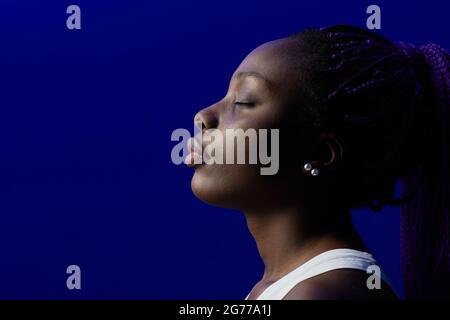 Portrait minimal de la jeune femme afro-américaine avec les yeux fermés sur fond violet en studio, espace de copie Banque D'Images