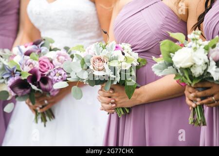 Demoiselles d'honneur roses et robes de vioilet tenant des arrangements floraux. Gros plan de la fête de la mariée avec des bouquets. Banque D'Images