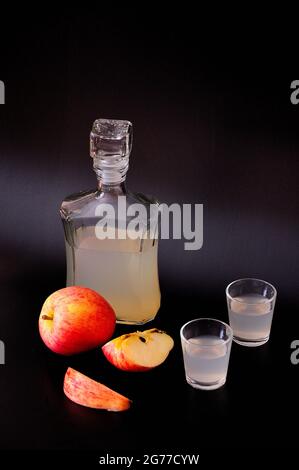 Calvados de pomme dans une bouteille et deux verres, fruits mûrs coupés en morceaux à côté d'un fond noir. Gros plan. Banque D'Images