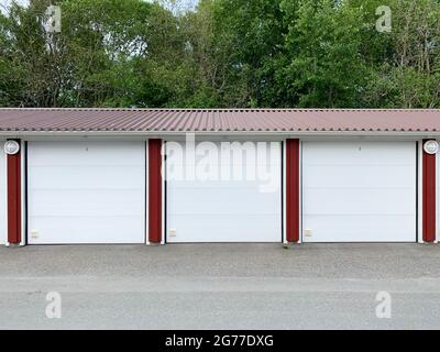 Trois portes de garage, parkings, avec place pour voitures. Barrières blanches, route pavée et arbres. Banque D'Images