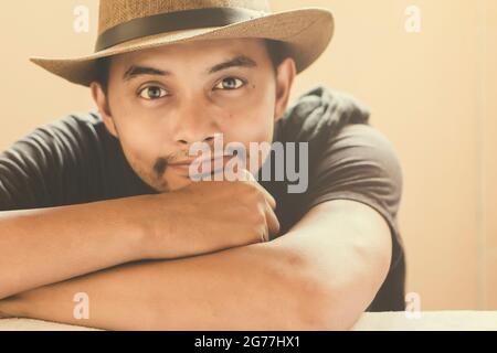 Beau homme assis souriant sous une lumière chaude. Style cowboy avec une moustache et un chapeau Banque D'Images