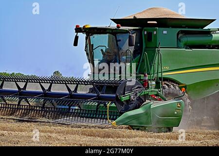 Avec sa trémie pleine de 300 boisseaux de blé d'hiver, une moissonneuse-batteuse S770 John Deere avec une barre de coupe 735FD fixée dans les barres de coupe avant à une remorque de tracteur à grains en vrac en attente pour transférer sa première charge de grain récolté dans le lit du camion pour un transport ultérieur vers Crédit local de la coopérative de céréales : Mark Reinstein / MediaPunch Banque D'Images