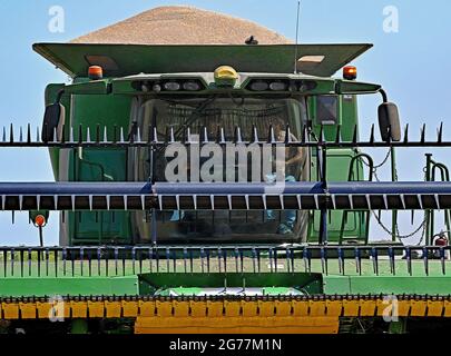 Avec sa trémie pleine de 300 boisseaux de blé d'hiver, une moissonneuse-batteuse S770 John Deere avec une barre de coupe 735FD fixée dans les barres de coupe avant à une remorque de tracteur à grains en vrac en attente pour transférer sa première charge de grain récolté dans le lit du camion pour un transport ultérieur vers Crédit local de la coopérative de céréales : Mark Reinstein / MediaPunch Banque D'Images