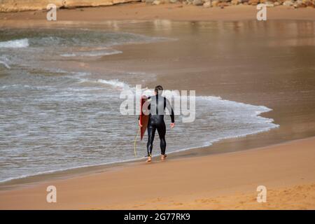 Vue arrière de l'homme australien surfeur marchant le long de Palm Beach à Sydney portant son surf, Australie Banque D'Images