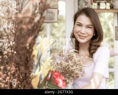 Mignonne belle asiatique d'âge moyen femme fleuriste propriétaire d'organisation d'un bouquet de fleurs prêt à vendre pour les clients. Photo traitée dans un style de film Banque D'Images