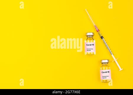 Flacons et seringues de vaccin contre le coronavirus Covid-19 placés sur fond jaune avec espace de copie. Vue du dessus et plan de pose à plat. Banque D'Images