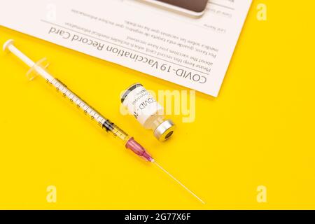 Flacon de vaccin et de seringue Covid-19 du coronavirus placé sur fond jaune et carte du dossier vacciné avec espace pour les copies. Concept de diffusion d'un cur Banque D'Images