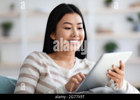 Happy Asian Female Shopping en ligne sur la tablette numérique tout en se relaxant à la maison Banque D'Images