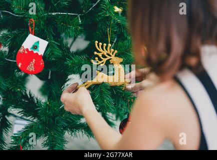 Vue arrière de la femme décorant et organisant l'arbre de Noël à la maison et se préparant pour les vacances d'hiver. Banque D'Images