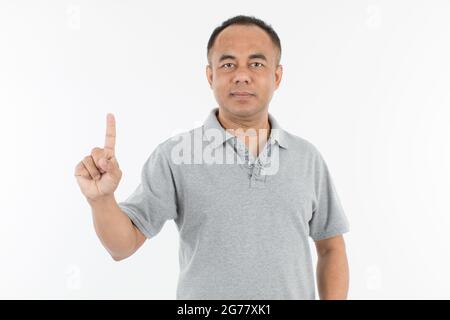 Portrait d'un homme asiatique âgé d'âge moyen dans un tissu gris clair levant et montrant un doigt. Isoler sur fond blanc. Banque D'Images