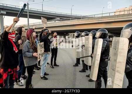 Groupe de jeunes manifestants masques tenant des panneaux et debout devant des gardes de police avec des boucliers Banque D'Images