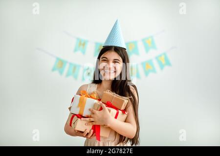 Une jeune fille indienne surjoyée dans un chapeau d'anniversaire tenant un tas de boîtes-cadeaux à l'intérieur Banque D'Images