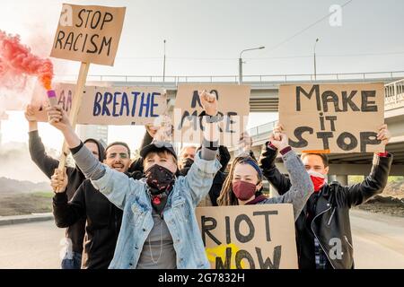 Groupe de jeunes rebelles multiethniques en colère se déplaçant avec des panneaux de carton sous les ponts et luttant pour l'égalité des droits pour toutes les races Banque D'Images