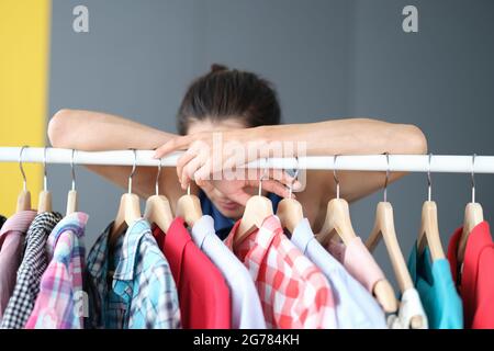 La femme pensive se tient près d'un cintre avec des vêtements Banque D'Images