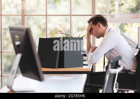 Le jeune homme d'affaires caucasien est assis près de la boîte d'appartenance et se sent stressé et utilise la main tenant son front après avoir été tiré pendant ECON Banque D'Images