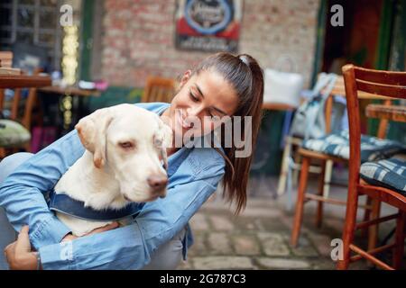 un chien charmant embrassé par une jeune femme de race blanche adulte qui lui sourit et le regarde Banque D'Images