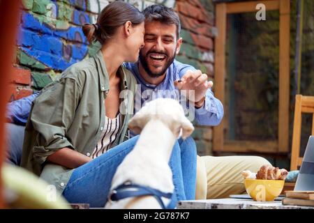 jeune couple caucasien s'amuser avec leur chien dans un café en plein air, nourrissant leur animal de compagnie, labrador retriever. Banque D'Images