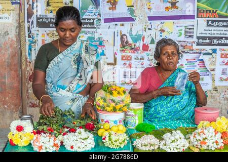 Les femmes indiennes au marché de la vente de guirlandes de fleurs comme l'offrande de temple de pooja devant des affiches colorées, Tamil Nadu, Inde Banque D'Images