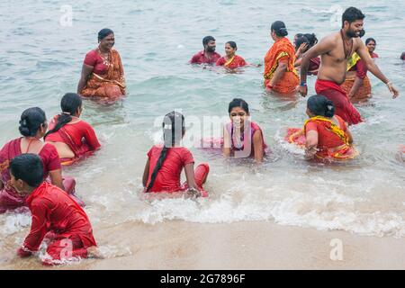 Groupe de fidèles hindous portant des vêtements rouges se baignant dans l'océan, Kanyakumari, Laccadive Sea, Tamil Nadu, Inde Banque D'Images