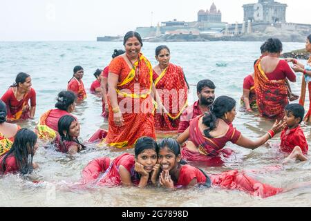 Groupe de fidèles hindous portant des vêtements rouges se baignent dans la mer de Laccadive devant le monument commémoratif Vivekananda Rock, Kanyakumari, Tamil Nadu, Inde Banque D'Images