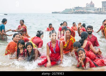 Groupe de fidèles hindous portant des vêtements rouges se baignant devant le monument commémoratif Vivekananda Rock, Kanyakumari, Laccadive Sea, Tamil Nadu, Inde Banque D'Images