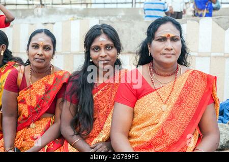 Gros plan de trois femelles indiennes portant des saris rouge/orange assis sur le mur à Kanyakumari, Tamil Nadu, Inde Banque D'Images