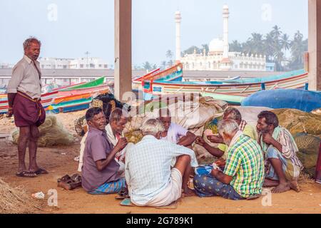 Groupe de pêcheurs hors service assis sur des cartes au sol avec la mosquée juma masjid en arrière-plan, Vizhinjam, Kerala, Inde Banque D'Images