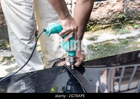 Ouvrier perçant la tôle de polycarbonate de toit avec la vis sur le cadre de structure Banque D'Images