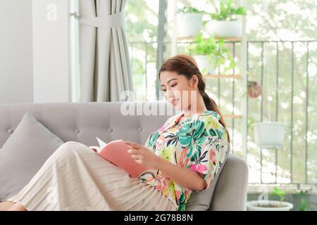 Femme lit le livre couché sur le canapé gris Banque D'Images