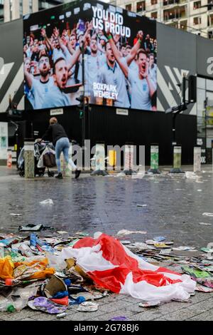 Wembley Park, Royaume-Uni. 12 juillet 2021. Immense écran LED « You'as US Proud » derrière une pile de litière dont un drapeau anglais. Des milliers de fans d'Angleterre ont quitté le parc Wembley couvert de détritus et sentant comme une brasserie après le comportement ahurant d'hier, avant, pendant et après la finale Euro 2020 entre l'Italie et l'Angleterre au stade Wembley. L'équipe de nettoyage a travaillé tout au long de la nuit pour ranger les déchets, y compris les drapeaux jetés, les panneaux, les bouteilles de bière et les canettes, les sacs en verre et en plastique cassés. Amanda Rose/Alamy Live News Banque D'Images