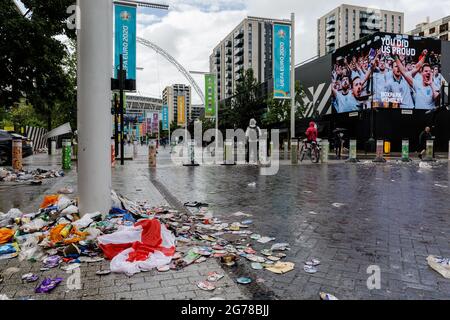 Wembley Park, Royaume-Uni. 12 juillet 2021. Immense écran LED « You'as US Proud » derrière une pile de litière dont un drapeau anglais. Des milliers de fans d'Angleterre ont quitté le parc Wembley couvert de détritus et sentant comme une brasserie après le comportement ahurant d'hier, avant, pendant et après la finale Euro 2020 entre l'Italie et l'Angleterre au stade Wembley. L'équipe de nettoyage a travaillé tout au long de la nuit pour ranger les déchets, y compris les drapeaux jetés, les panneaux, les bouteilles de bière et les canettes, les sacs en verre et en plastique cassés. Amanda Rose/Alamy Live News Banque D'Images