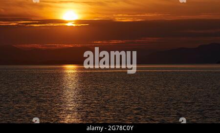 Iles Ioniennes, Ithaca, Île d'Odysseus, Frikes, lever du soleil, lumière du matin, humeur du matin, lever du soleil sur le continent, sunbeam sur la mer, ciel bleu à orange, rive grise de nuages sous le soleil Banque D'Images