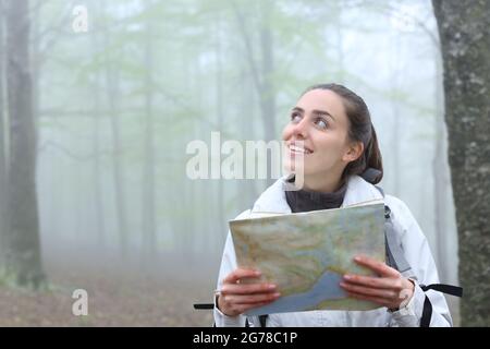 Happy Trekker tenant une carte en papier regardant à côté dans la nature un jour brumeux Banque D'Images