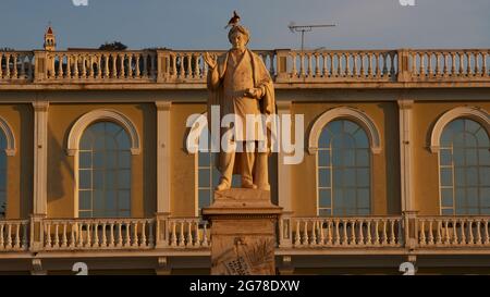 Zakynthos, ville de Zakynthos, place Solomos, statue du poète national Dionysios Solomos en face du Musée byzantin de la ville de Zakynthos, en arrière-plan quatre fenêtres voûtées du Musée byzantin, le pigeon se trouve à la tête de la statue, lumière du matin, étroite bande de ciel bleu clair au-dessus du musée et de la statue Banque D'Images